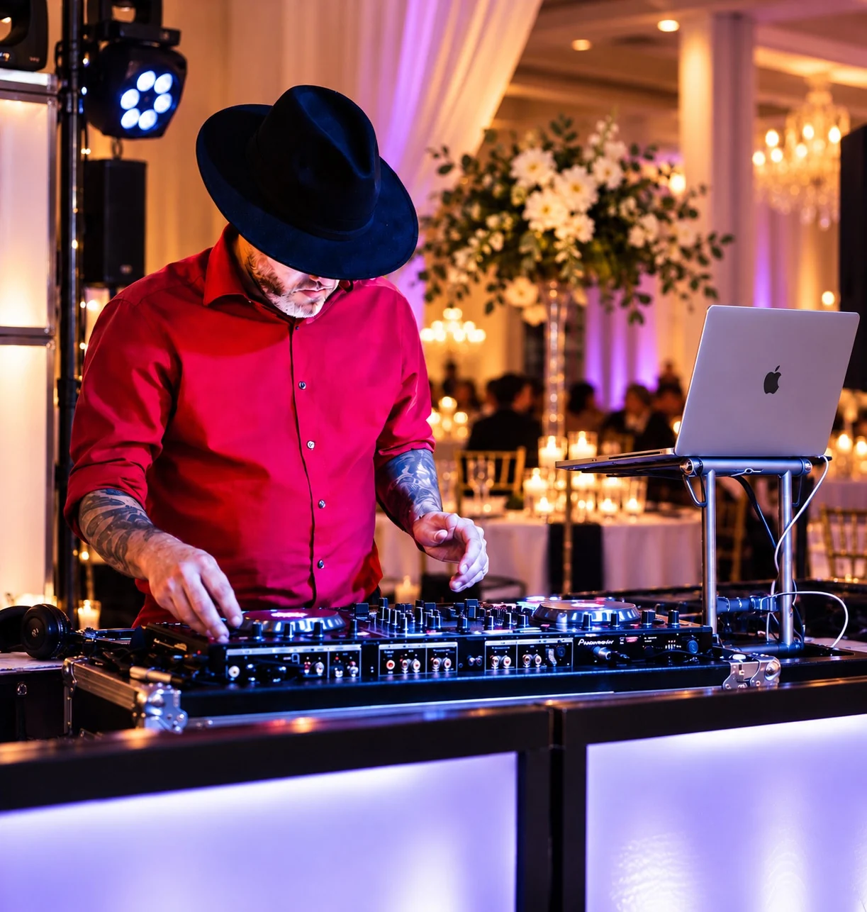 DJ Zach B in a red shirt and black hat mixing music at a wedding reception